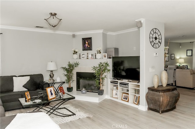 living room featuring light hardwood / wood-style flooring, a tiled fireplace, and crown molding