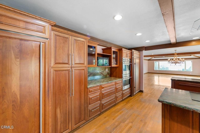 kitchen with an inviting chandelier, light hardwood / wood-style flooring, dark stone countertops, beam ceiling, and stainless steel double oven