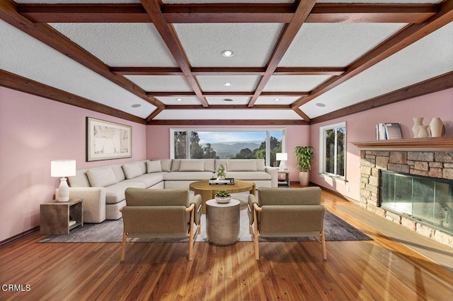 living room featuring beamed ceiling, hardwood / wood-style floors, a stone fireplace, and coffered ceiling