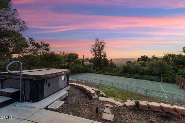 pool at dusk with a hot tub and tennis court