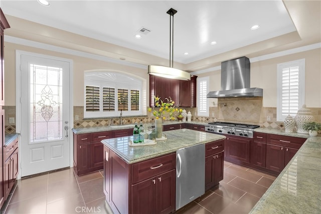 kitchen featuring light stone counters, appliances with stainless steel finishes, hanging light fixtures, and wall chimney range hood