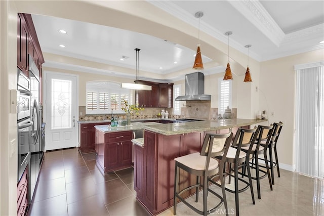 kitchen with wall chimney exhaust hood, hanging light fixtures, kitchen peninsula, and tasteful backsplash