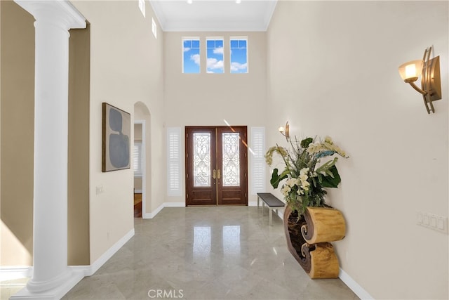 foyer featuring french doors, crown molding, ornate columns, and a high ceiling