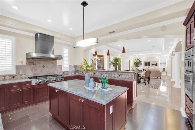 kitchen featuring appliances with stainless steel finishes, tasteful backsplash, wall chimney exhaust hood, pendant lighting, and a center island