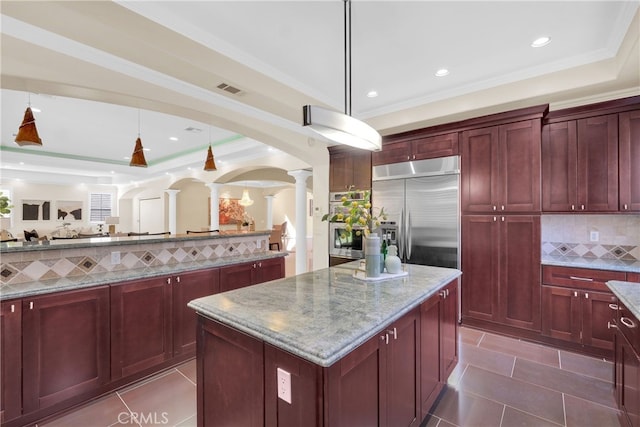 kitchen featuring a center island, hanging light fixtures, backsplash, appliances with stainless steel finishes, and ornate columns