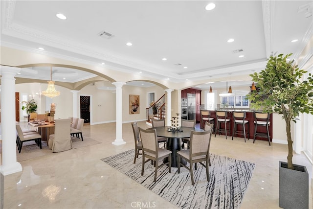 dining space with a tray ceiling, a chandelier, and ornate columns