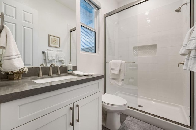 bathroom featuring a shower with shower door, toilet, and vanity