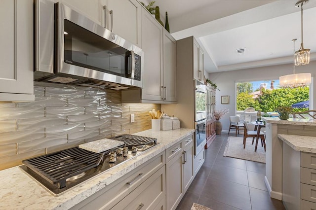 kitchen featuring light stone countertops, dark tile patterned flooring, appliances with stainless steel finishes, tasteful backsplash, and hanging light fixtures