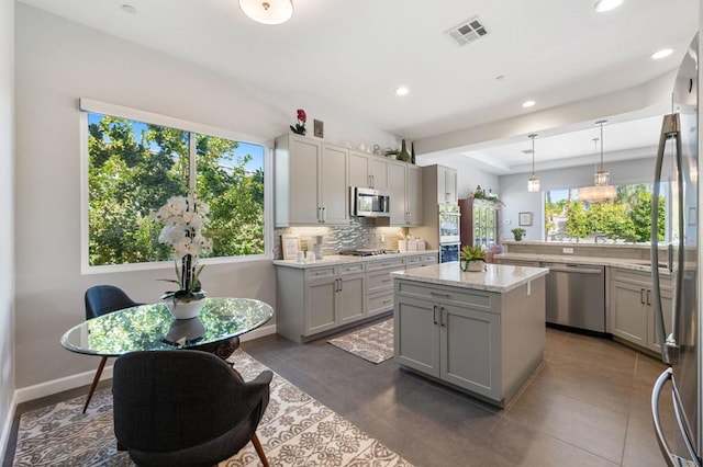 kitchen featuring gray cabinets, appliances with stainless steel finishes, decorative backsplash, hanging light fixtures, and a center island