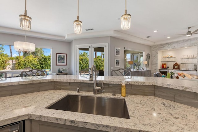 kitchen with decorative light fixtures, ceiling fan with notable chandelier, stainless steel dishwasher, sink, and light stone counters