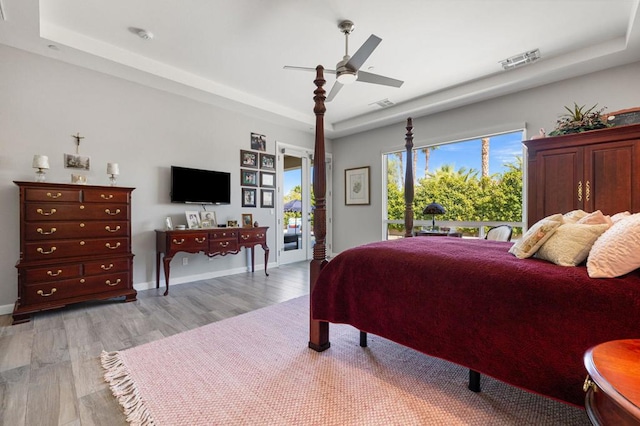 bedroom with ceiling fan, access to exterior, a raised ceiling, and light hardwood / wood-style floors