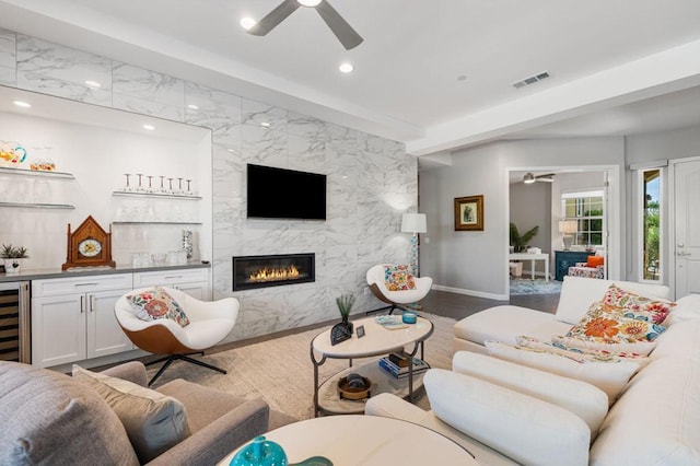 living room with ceiling fan, tile walls, beverage cooler, and a fireplace