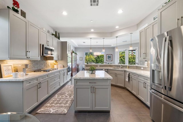 kitchen with backsplash, gray cabinets, sink, hanging light fixtures, and stainless steel appliances