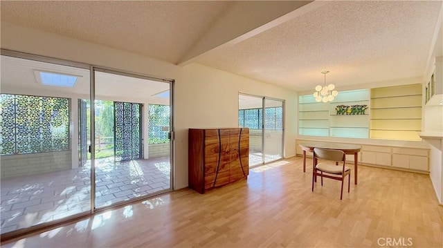 dining room with built in shelves, light hardwood / wood-style flooring, a textured ceiling, and a notable chandelier