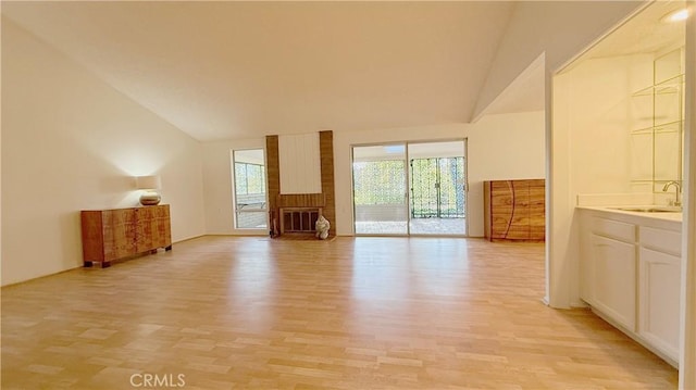 unfurnished living room with light wood-type flooring, vaulted ceiling, and sink