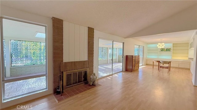 unfurnished living room featuring built in shelves, a brick fireplace, plenty of natural light, and an inviting chandelier