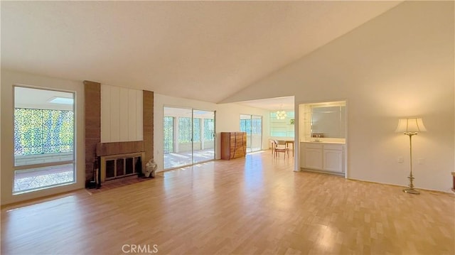 unfurnished living room with light hardwood / wood-style floors, high vaulted ceiling, a chandelier, and a fireplace