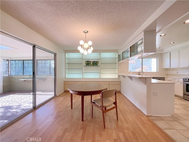 dining area with a textured ceiling, built in shelves, sink, a notable chandelier, and light hardwood / wood-style flooring