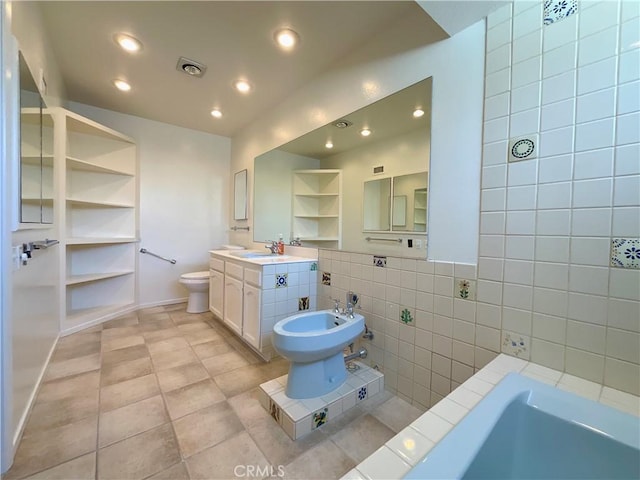 bathroom with vanity, tile walls, toilet, built in features, and a bidet