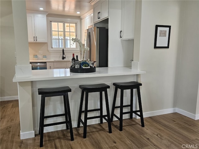 kitchen featuring a breakfast bar, dark hardwood / wood-style floors, white cabinetry, kitchen peninsula, and stainless steel appliances