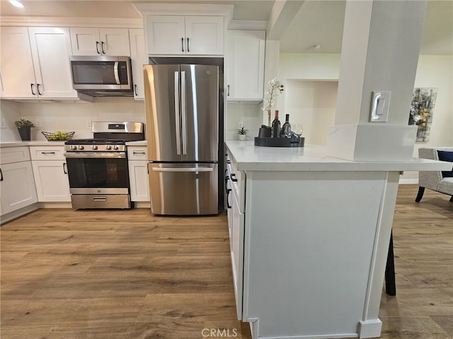 kitchen with white cabinets, light stone counters, light hardwood / wood-style floors, and appliances with stainless steel finishes