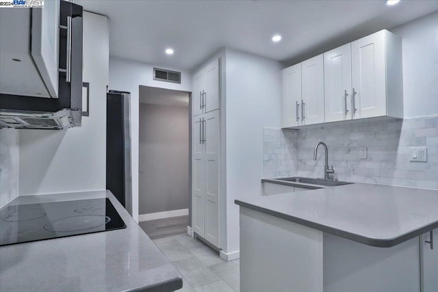 kitchen with black electric cooktop, white cabinetry, tasteful backsplash, kitchen peninsula, and sink