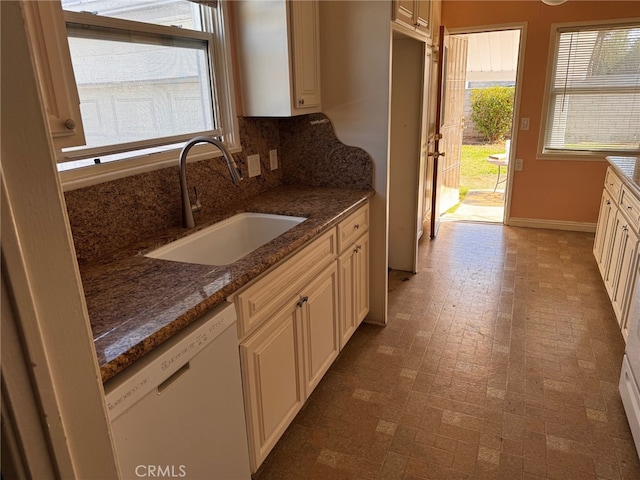 kitchen with white dishwasher, dark stone counters, sink, and tasteful backsplash