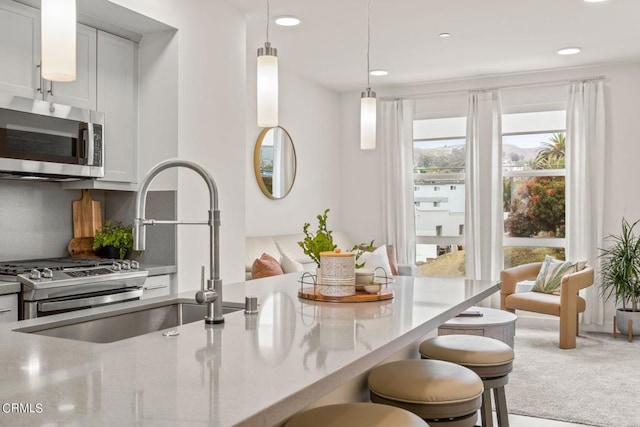 kitchen featuring carpet, a breakfast bar, stainless steel microwave, a sink, and hanging light fixtures