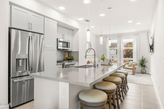 kitchen featuring a kitchen breakfast bar, stainless steel appliances, a sink, visible vents, and a kitchen island with sink