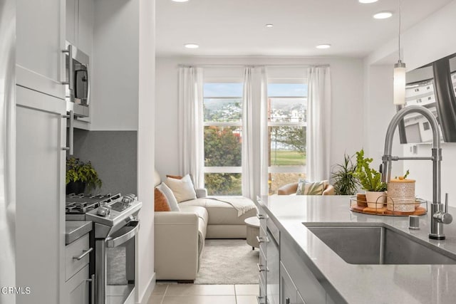 kitchen with light tile patterned flooring, light stone countertops, appliances with stainless steel finishes, a sink, and hanging light fixtures