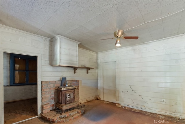 unfurnished living room with a wood stove and ceiling fan