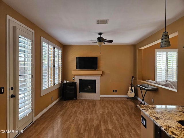 unfurnished living room with a tiled fireplace, ceiling fan, and hardwood / wood-style floors