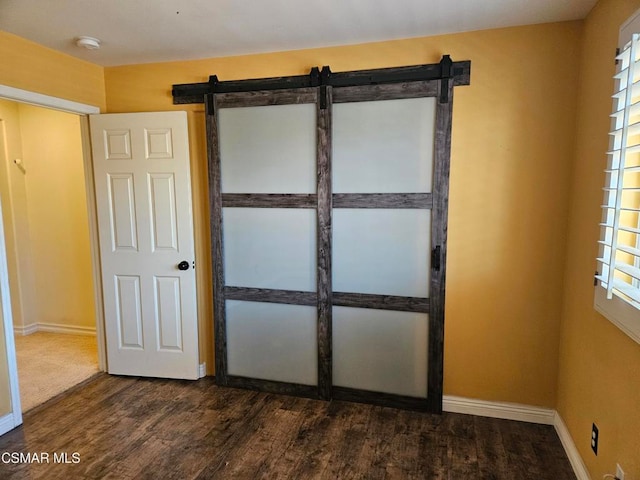 unfurnished bedroom featuring a barn door and dark hardwood / wood-style flooring