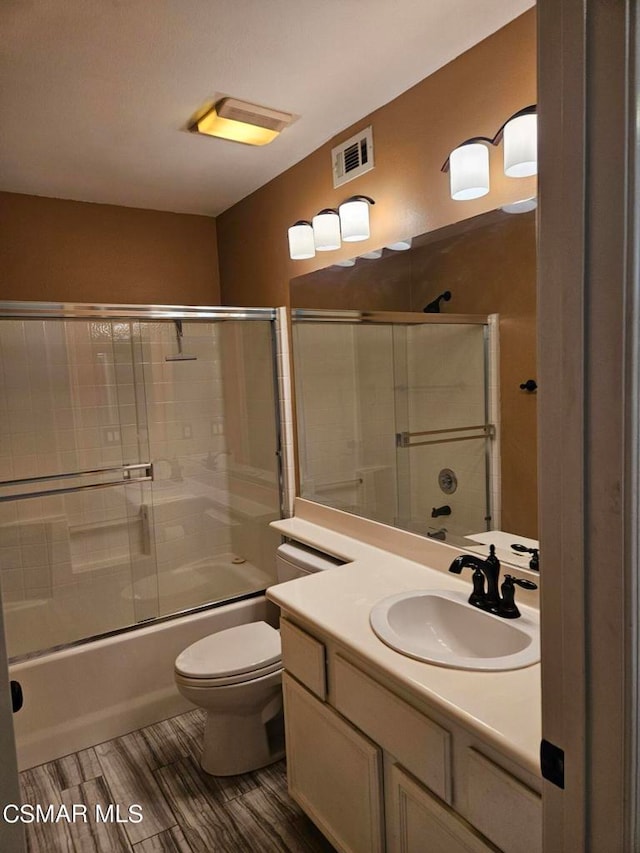 full bathroom with bath / shower combo with glass door, vanity, hardwood / wood-style floors, and toilet