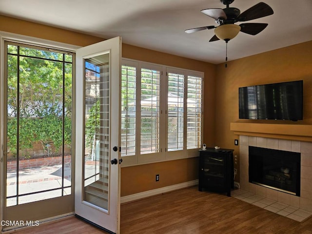 doorway to outside featuring a tile fireplace, wood-type flooring, ceiling fan, and plenty of natural light