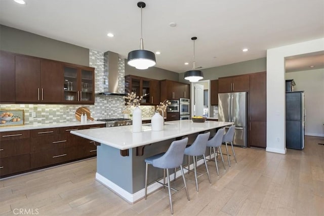 kitchen with stainless steel appliances, a breakfast bar, wall chimney range hood, and tasteful backsplash