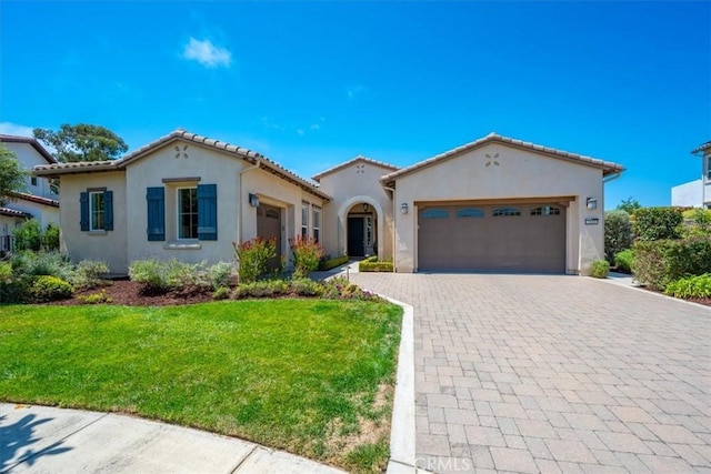 mediterranean / spanish-style home with a garage, a tiled roof, decorative driveway, a front lawn, and stucco siding