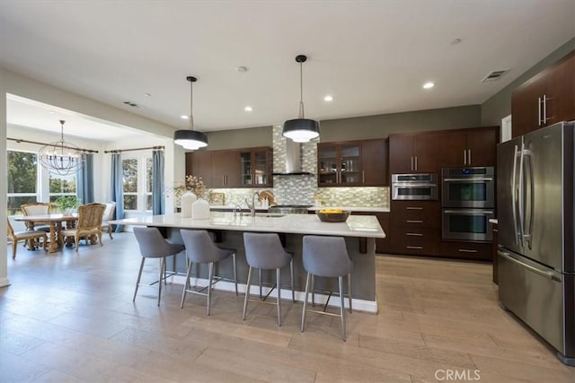 kitchen with wall chimney range hood, visible vents, appliances with stainless steel finishes, and light countertops