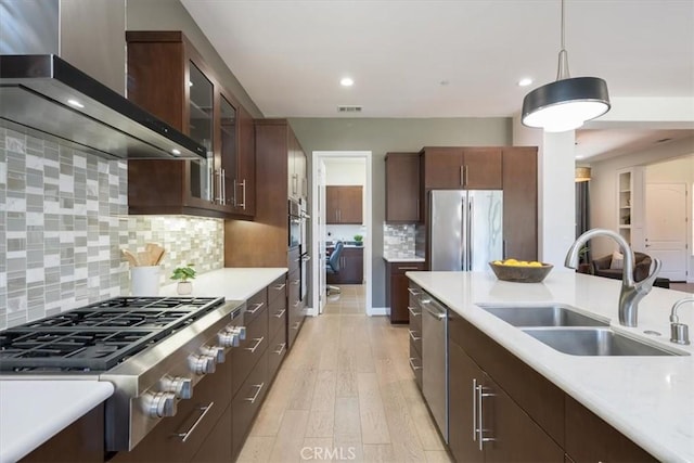 kitchen with wall chimney range hood, stainless steel appliances, a sink, and light countertops