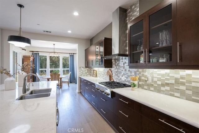 kitchen with stainless steel gas cooktop, a sink, decorative backsplash, wall chimney exhaust hood, and pendant lighting