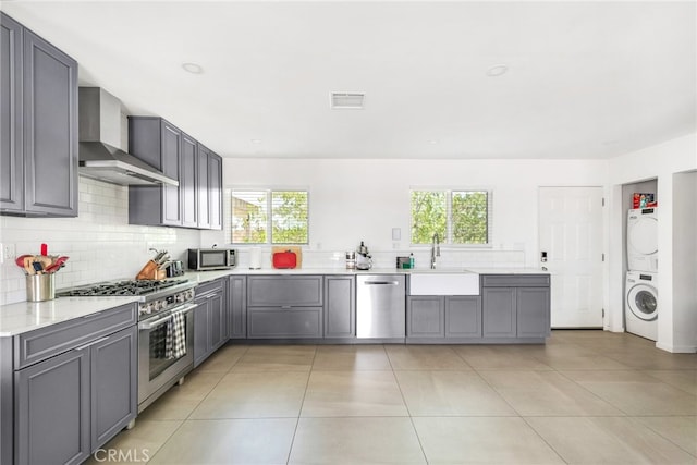 kitchen featuring wall chimney range hood, a healthy amount of sunlight, stainless steel appliances, and stacked washer and clothes dryer