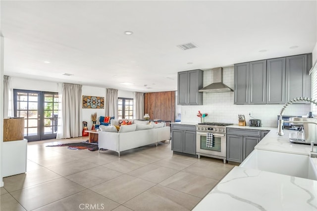 kitchen featuring french doors, wall chimney exhaust hood, stainless steel range, light stone countertops, and gray cabinets