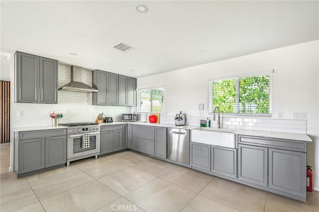 kitchen featuring gray cabinets, appliances with stainless steel finishes, wall chimney range hood, and light tile patterned floors