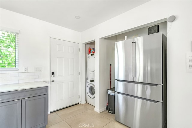 washroom featuring gray cabinets, stacked washer / drying machine, light stone counters, and light tile patterned floors