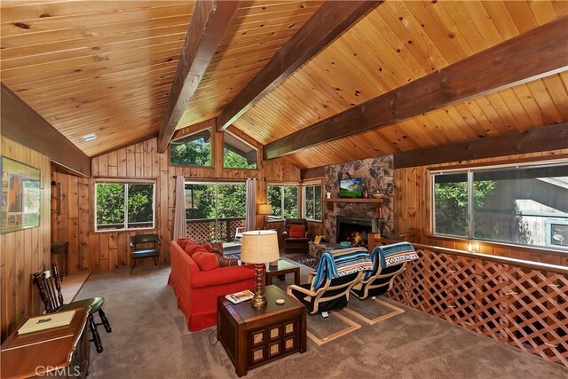 carpeted living room with vaulted ceiling with beams, wood walls, and a stone fireplace