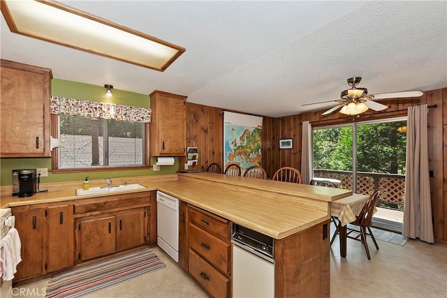 kitchen featuring ceiling fan, wood walls, kitchen peninsula, sink, and white dishwasher