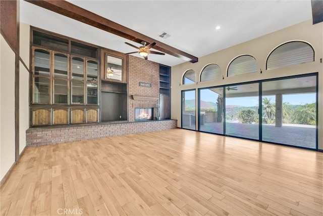 unfurnished living room with ceiling fan, beamed ceiling, light hardwood / wood-style floors, and a brick fireplace