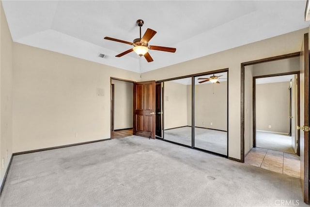 unfurnished bedroom featuring a raised ceiling, ceiling fan, a closet, and light colored carpet