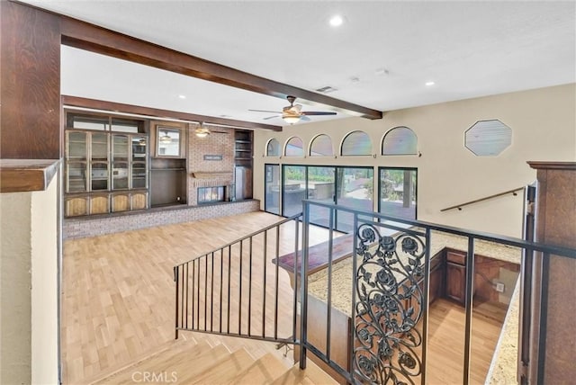 stairs with wood-type flooring, a brick fireplace, ceiling fan, and beam ceiling