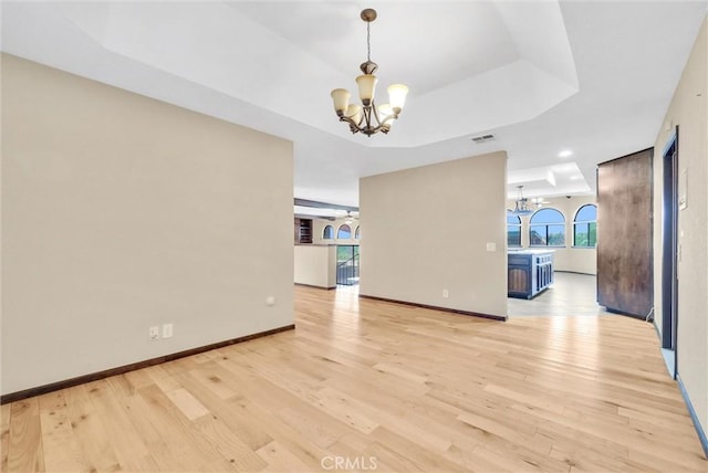 interior space featuring light hardwood / wood-style floors, a tray ceiling, and an inviting chandelier